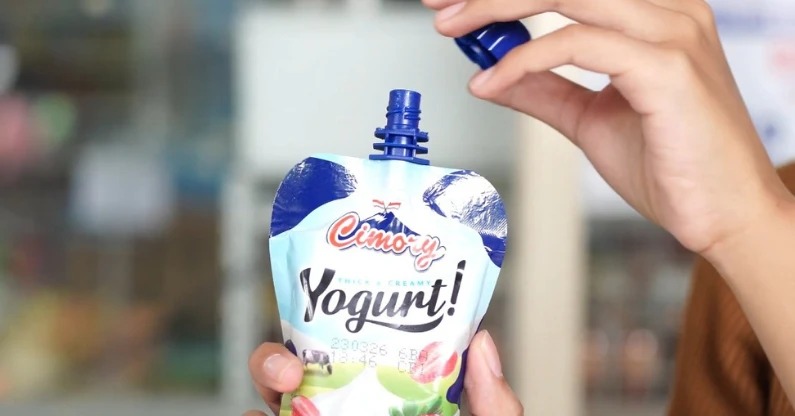 Hand opening a Cimory Squeeze Yogurt pouch, packaging close-up